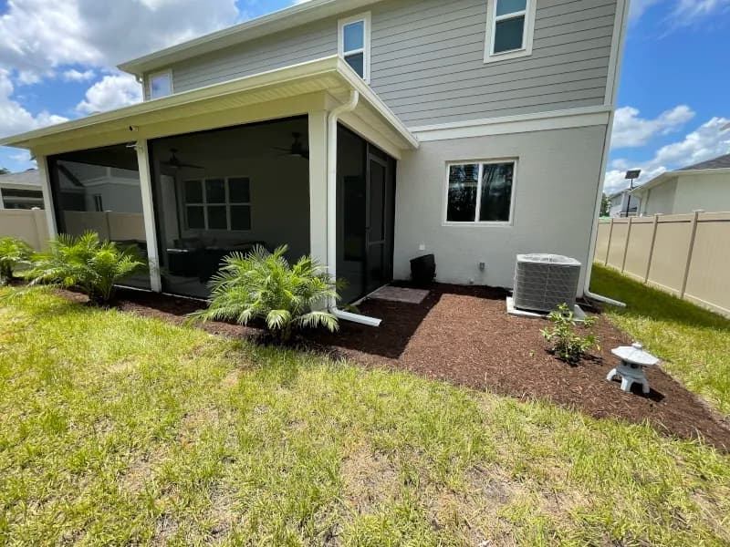 Backyard landscaping with brown mulch, new plants and a stone lantern by the lanai