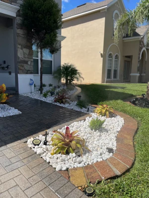 White river-rock bed with bromeliads and solar lights along a paver driveway