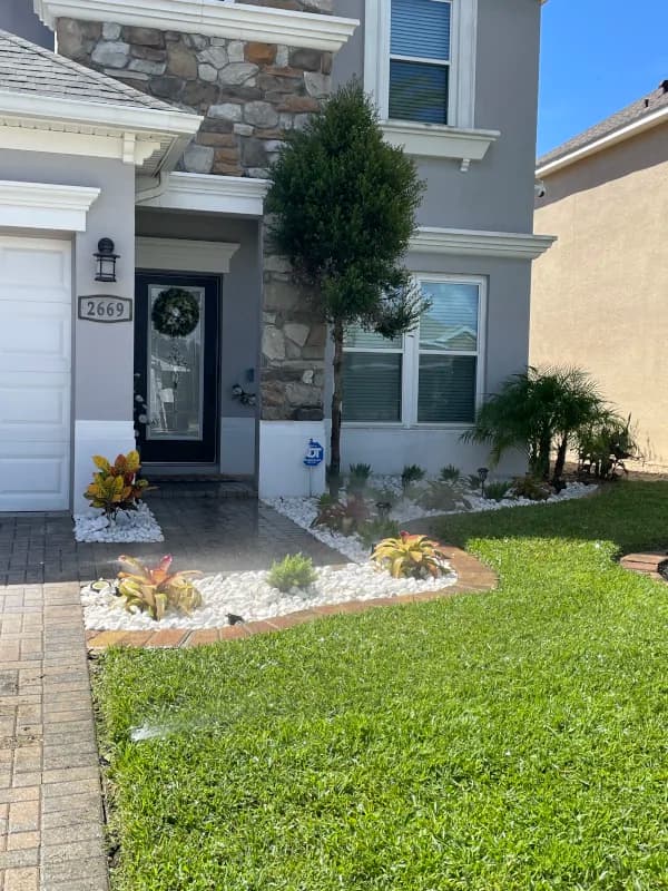 Front entry with a white rock border, tropical plants and a freshly cut lawn