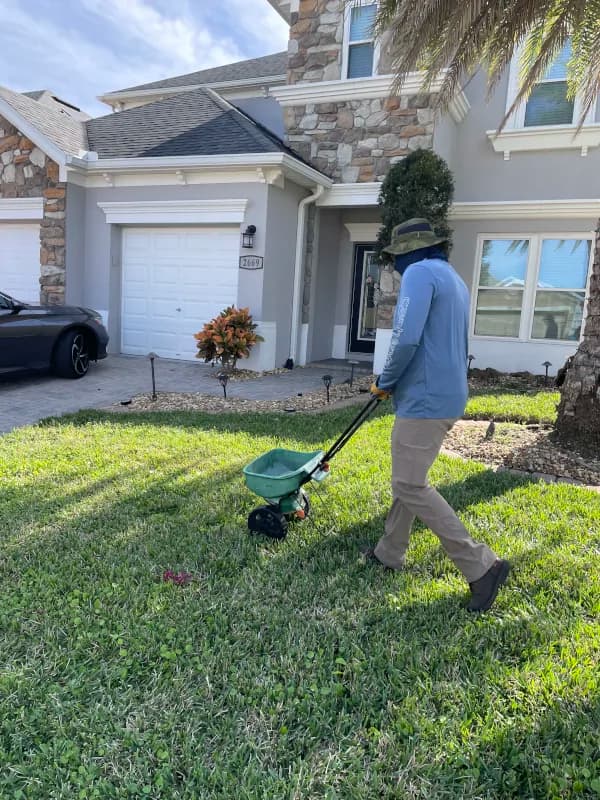 Crew member spreading fertilizer with a push spreader on the front lawn of a stone-accent home