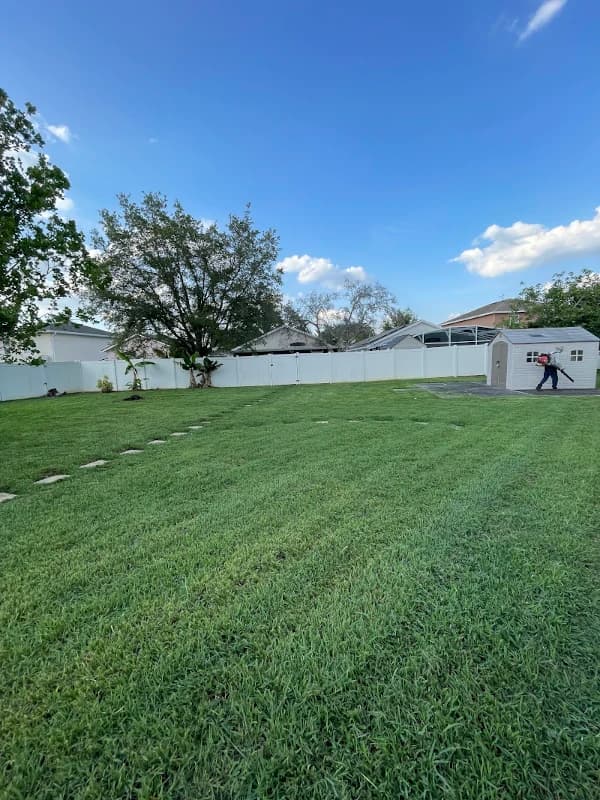 Crew member using a leaf blower beside a shed after mowing a large fenced backyard