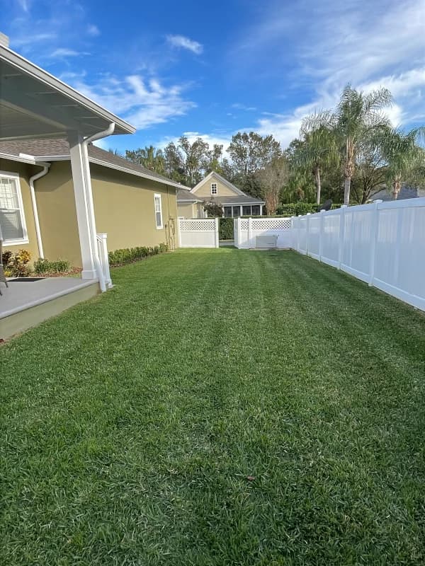 Striped, freshly mowed side yard between a covered porch and a white vinyl fence