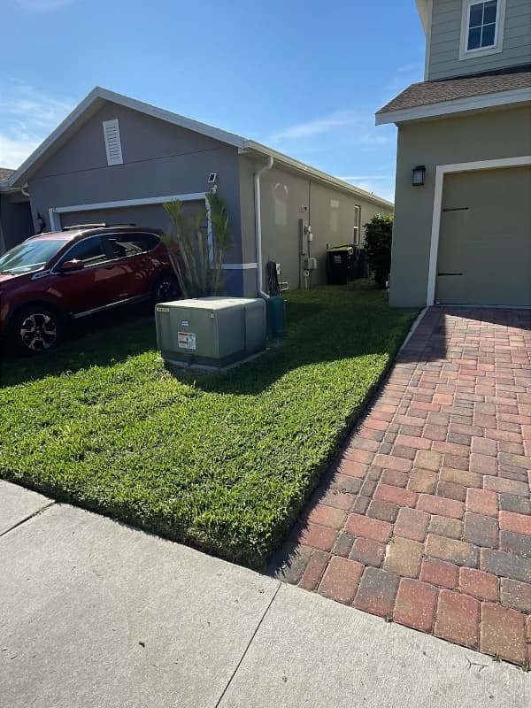 Small front lawn mowed and edged along a red paver driveway