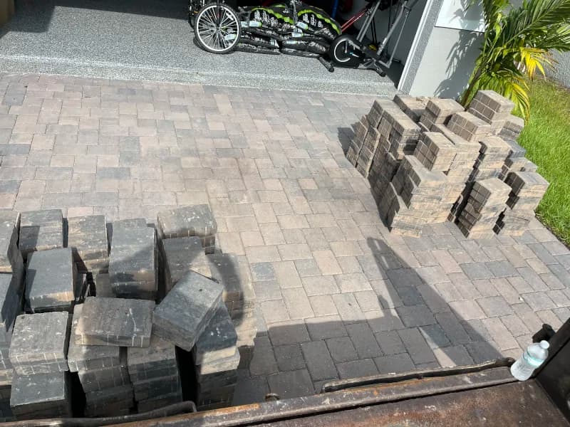 Paver driveway repair in progress with stacked pavers beside a garage