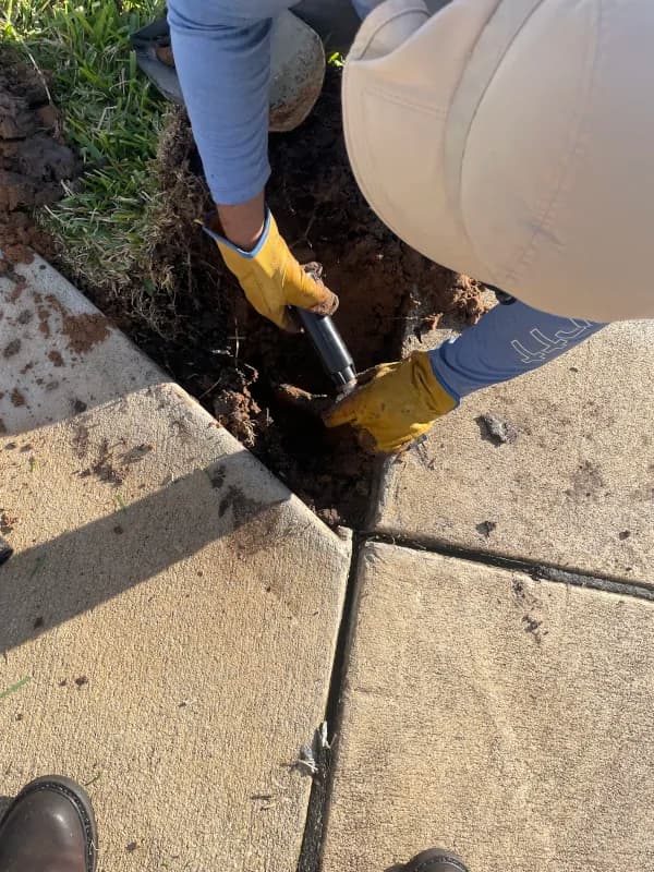 Crew member digging beside a sidewalk to reach a sprinkler line