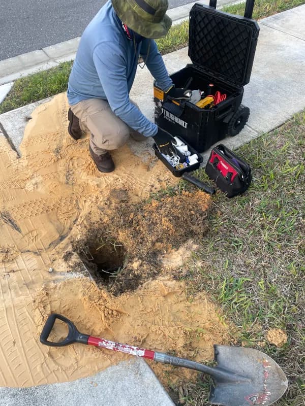 Technician with tools beside a dug-out sprinkler repair in a yard