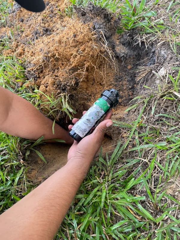 Crew member setting a new sprinkler head into the lawn