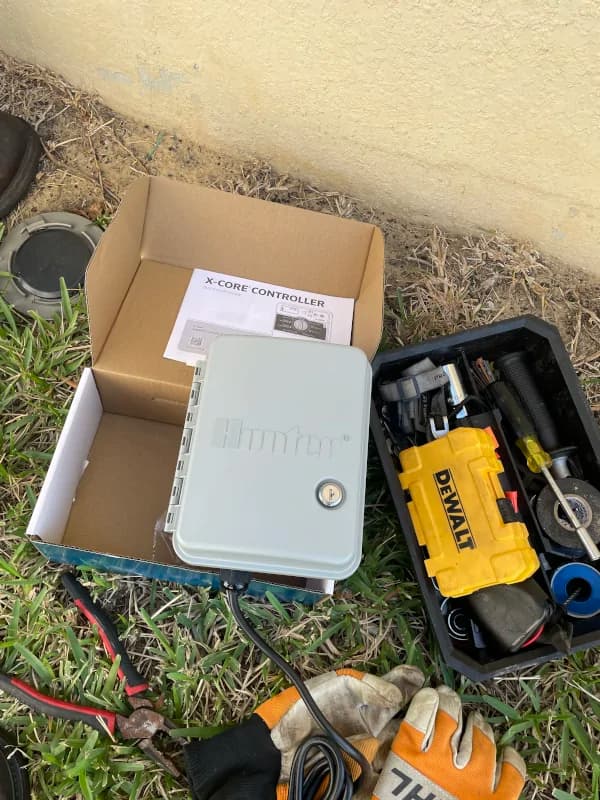 New sprinkler controller and tools laid out on the grass before installation