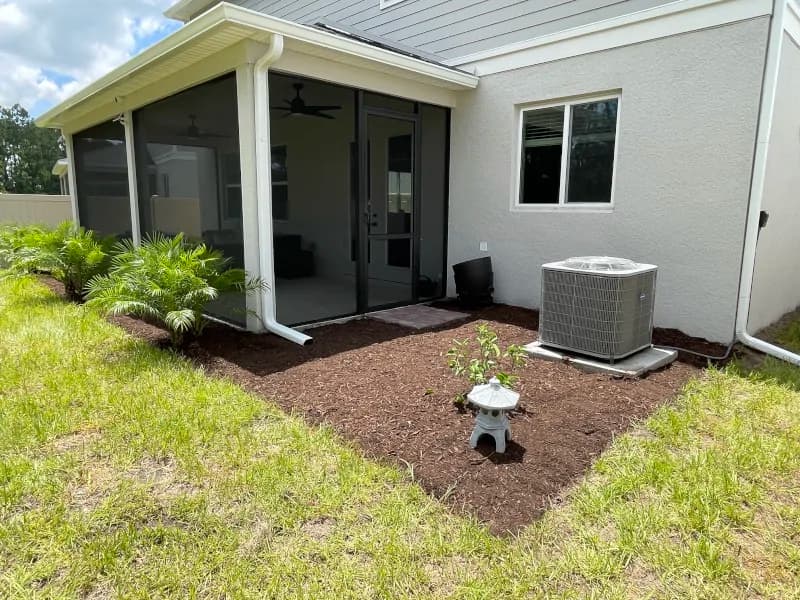 Brown mulch bed with new plants and a garden lantern beside a screened lanai