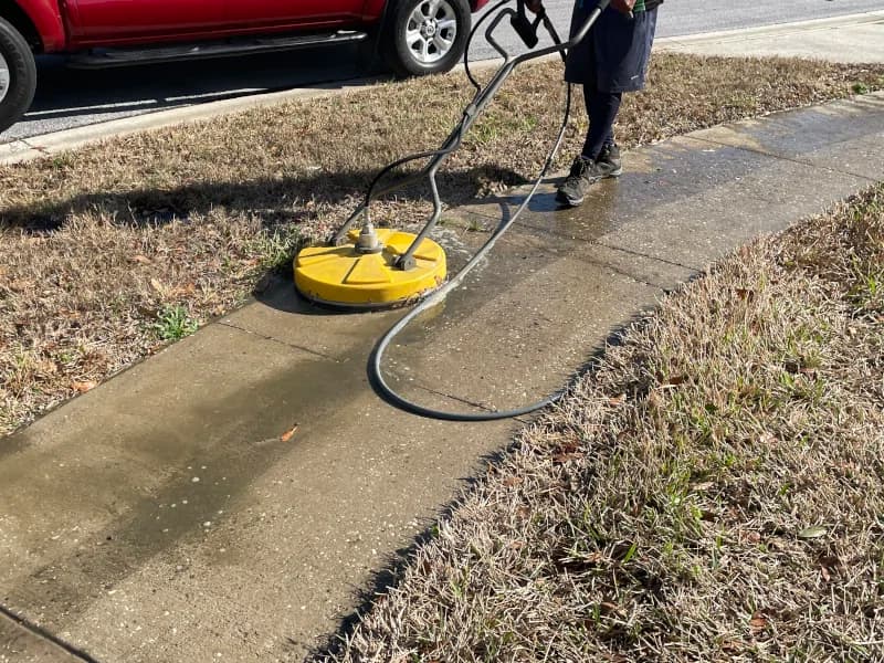 Pressure washing a sidewalk with a surface cleaner, the clean strip showing behind it
